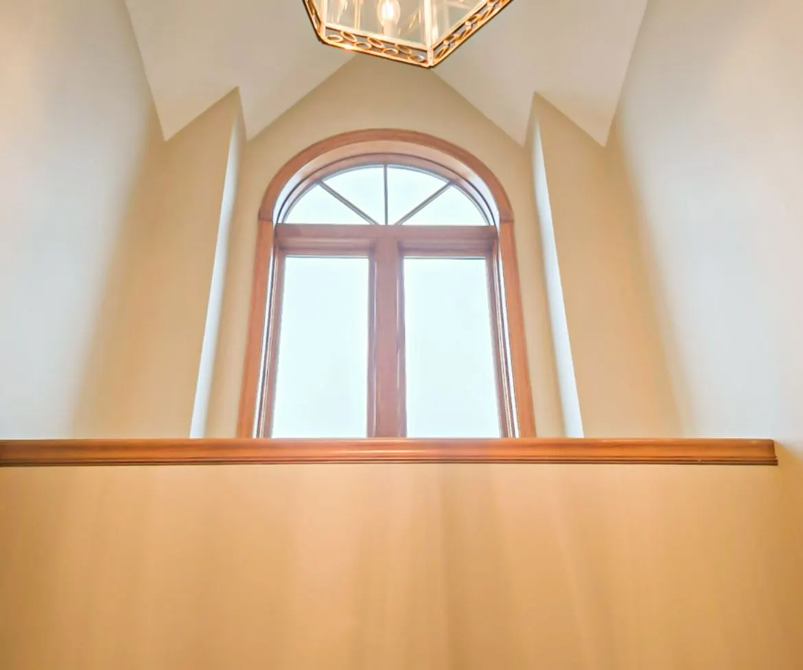 Arched window with wood trim in a stairwell with a ceiling light above