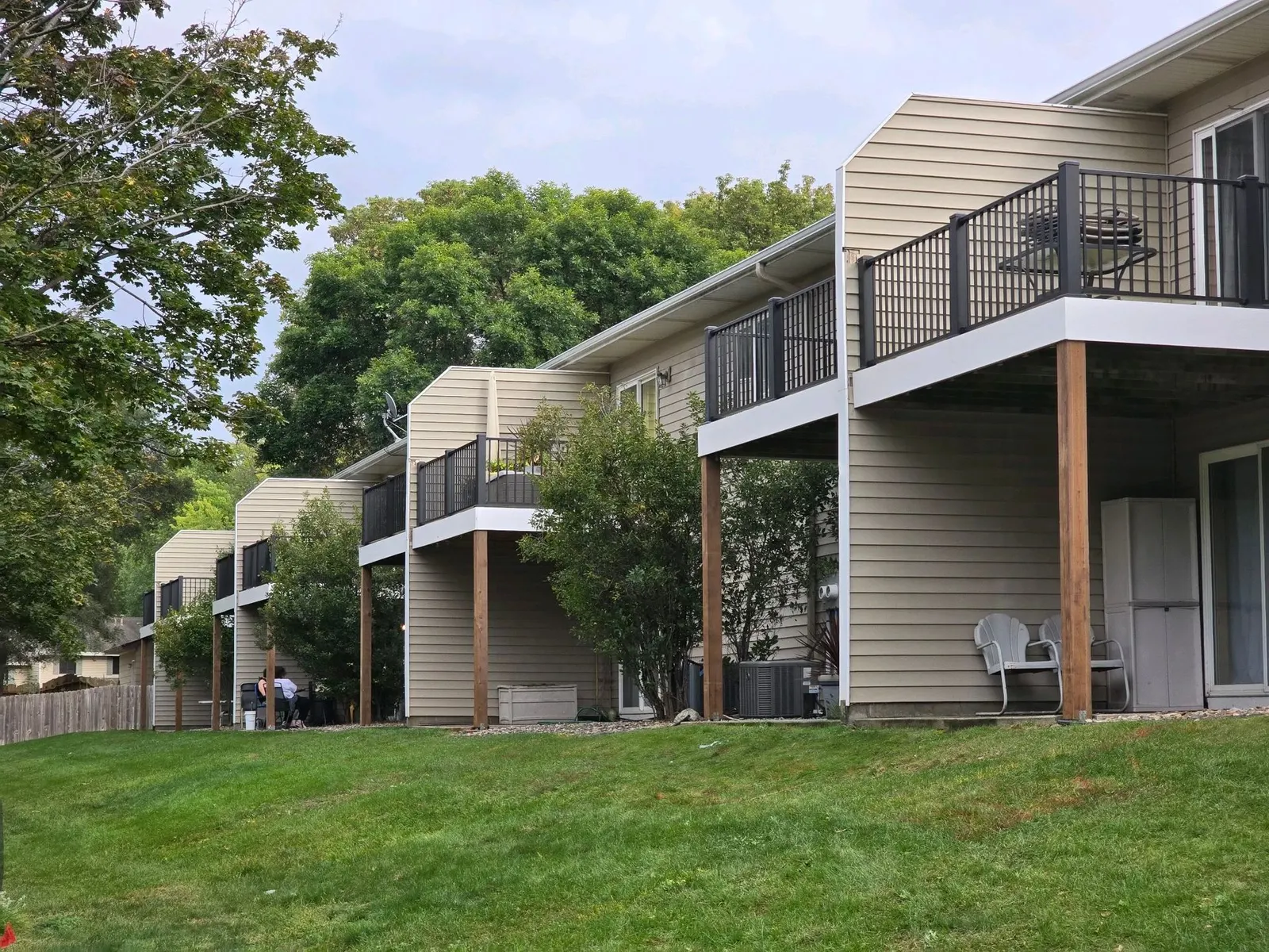 Back of a row of townhomes with tan siding, balconies, and a green lawn